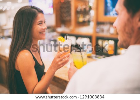 Bar drinking cocktails dating couple lovers talking with drinks at restaurant at night. People at restaurant with alcoholic cocktail beverage. Asian woman smiling.