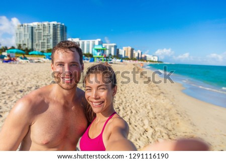 Miami beach selfie couple on summer holiday. Interracial young adults sun tanning on south beach, Florida, USA. Asian woman, Caucasian man.