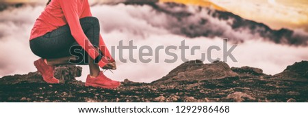 Runner smartwatch woman getting ready for trail run in high cold clouds mountains background tying up running shoes laces. Fitness and sports motivation healthy lifestyle. Banner panoramic crop.