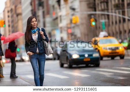 Young Asian professional woman walking home commuting from work in New York city street. Urban people lifestyle commuter in NYC traffic rain day. Chinese girl with purse and headphones for commute.