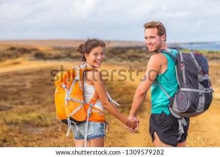 Happy young couple tourists in love holding hands walking on trek hike with backpacks. Hikers on nature travel hiker trail destination smiling happy. Interracial relationship.