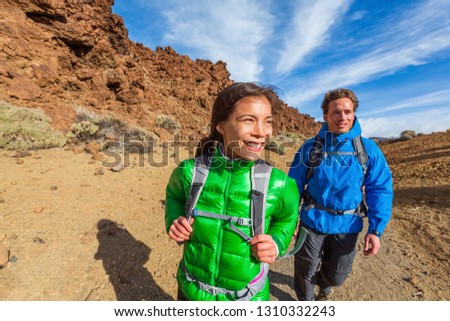 Happy hikers on mountain climb hike trekking with cold jackets and backpacks healthy active lifestyle. Young Asian woman with Caucasian man smiling walking outdoors.