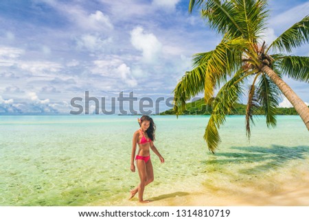 Luxury beach Tahiti Bora Bora bikini woman swimming in paradise getaway vacation. Beautiful Asian swimsuit model relaxing walking in turquoise ocean water in secluded island.