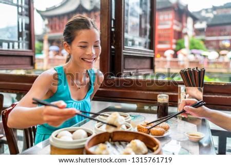 Chinese woman eating at Shanghai restaurant Xiao long bao / xiaolongbao soup dumplings typical food China travel vacation. Asia tourist girl eating Shanghainese steamed dumpling buns with chopsticks.