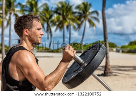 Outdoor calisthenics gym park male athlete working out on T-bar outside in summer. Man workout strength training arms biceps muscles with heavy weights.