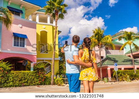 Couple on winter vacation taking pictures of pastel colored beach houses cottages in tropical holiday destination Fort Myers, Florida. Man tourist taking picture with phone.