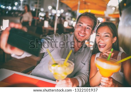 Fun date night out young people taking selfie of themselves drinking giant margaritas cocktails party couple going out on Miami Ocean drive restaurant. Funny drinks outdoor terrace travel lifestyle.