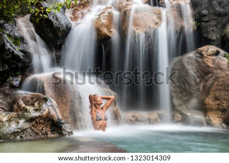 Waterfall woman relaxing swimming in water. Spa wellness relaxation health concept in nature water in tropical travel vacation background. Sexy bikini body Asian girl swimming.