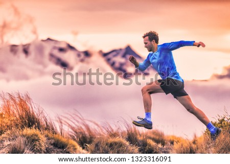 Sport runner trail running man in mountains cold clouds and hills. Male athlete training cardio jumping against altitude sky background.