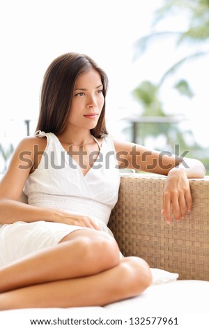 Confident serious sophisticated woman thinking and looking outdoors in luxury setting. Beautiful young multicultural Asian Caucasian female model in white dress relaxing outside.