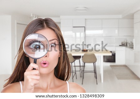 Home shopping funny inspection woman searching through magnifying glass at kitchen furniture. Deal hunting bargain hunter Asian girl looking at real estate new homeowner inspecting interior design.