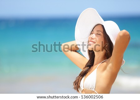 Relaxing beach woman enjoying the summer sun happy standing in a wide sun hat at the beach with face raised to the sunlight. Head and shoulder portrait. Multicultural Asian Caucasian in enjoyment.