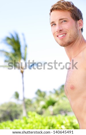 Handsome man on tropical beach smiling happy. Good-looking guy standing shirtless enjoying summer holidays on beach. Caucasian male model in his .
