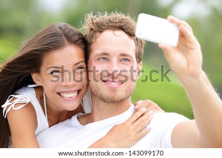 Couple Fun Taking Self-Portrait Picture Photos With Mobile Smart Phone Or Pocket Camera Outdoors. Happy Multiracial Young Couple In Love Taking Pictures Together On Summer Vacation. Man And Woman