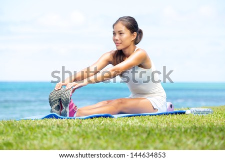 Woman training fitness stretching legs exercise outside by the ocean sea Beautiful fit female fitness girl model sitting on grass doing stretch exercising after workout Mixed race Asian female model Woman training fitness stretching legs exercise outside by the ocean sea Beautiful fit female fitness girl model sitting on grass doing stretch exercising after workout Mixed race Asian female model