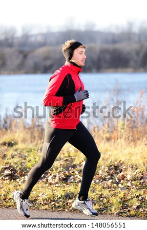 Running man jogging in autumn outdoor on cold day wearing long tights and sporty jogging outfit. Fit male fitness athlete model training outdoor in fall. Full body length of jogger.