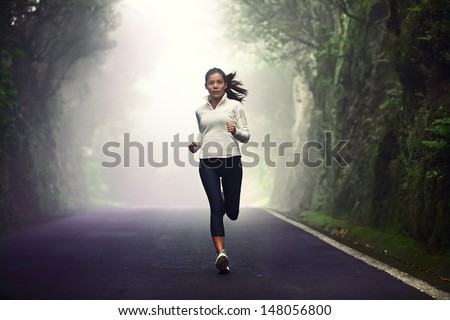 Woman running on road. Female runner jogging on mountain road training for marathon. Fit girl fitness athlete model exercising outdoor.