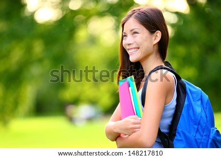 University / college student girl looking happy smiling with book or notebook in campus park. Beautiful young mixed race Asian Chinese / Caucasian young woman female model.