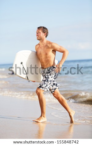 Beach water sports surfing man with body surfboard running happy during summer holidays vacation on tropical beach on sunny day with sunshine. Handsome fit male fitness sport model. Hawaii, USA.
