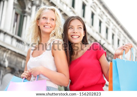 Shopping girls - women shoppers holding shopping bags in Venice. Portrait of Multiracial girlfriends smiling happy together having fun on San Marco Square, Venice, Italy. Caucasian and Asian models.