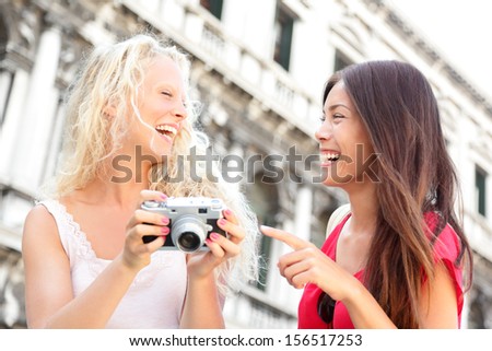 Women friends - girlfriends laughing having fun happy outside. Multiracial friends, Asian woman and Caucasian blonde girl looking at pictures on camera, Travel on San Marco Square, Venice, Italy