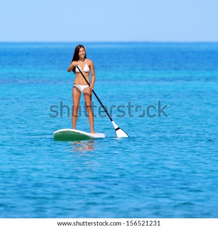 Paddleboarding beach woman on stand up paddleboard surfboard surfing in ocean sea on Big Island, Hawaii. Beautiful young multiracial Asian Caucasian woman in bikini doing water sports on vacation.