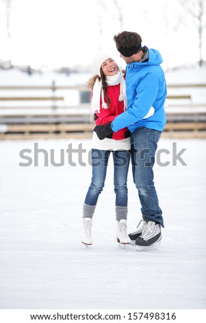 Ice skating couple on date in love iceskating and embracing. Young couple embracing on ice skates outdoors on open air rink in snowy winter landscape. Multiracial couple, Asian woman, caucasian man.
