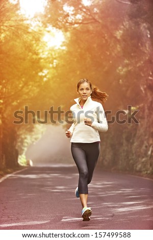 Young woman running Female runner jogging on misty road with the early morning at sunrise with sun breaking through the trees as she trains during a fitness workout Young woman running Female runner jogging on misty road with the early morning at sunrise with sun breaking through the trees as she trains during a fitness workout