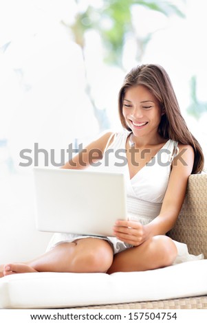Laptop woman using computer in Sofa. Beautiful happy girl looking at screen smiling sitting casual having fun on internet. Young female Asian Caucasian mixed race model outdoors.