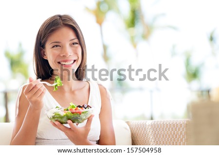 Healthy lifestyle woman eating salad smiling happy outdoors on beautiful day. Young female eating healthy food outside in summer dress laughing and relaxing in sofa. Pretty multiracial model.