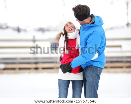 Ice skating romantic couple on date iceskating embracing. Young couple holding hands on ice skates outdoors on open air rink in snowy winter landscape. Multiracial couple, Asian woman, caucasian man