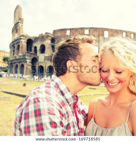 Love - Couple Kissing Having Fun In Rome By The Colosseum. Romantic Tourists On Holidays Vacation Travel And Man Kissing Woman On Cheek. Beautiful Blonde Girl And Guy In 20s. Coliseum, Rome, Italy.