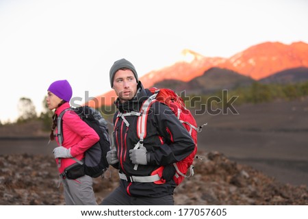 Hiking people on mountain. Hiker couple walking with backpacks outdoors in high altitude. Young man hiker in focus trekking at sunset on volcano Teide, Tenerife, Canary Islands, Spain.