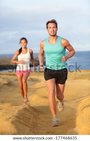 Runners couple jogging for fitness running in beautiful landscape nature outdoors. Young female and male sports athletes training cross-country trail running. Asian woman, Caucasian man,