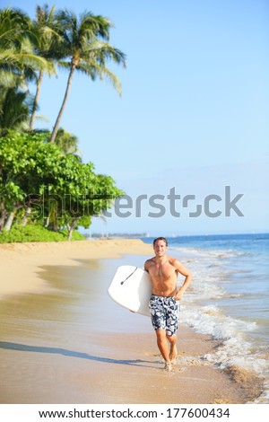 Beach lifestyle man surfer with surfing bodyboard running in water on tropical beach. Handsome male model in swimwear having summer vacation holidays fun on Kaanapali beach, Maui, Hawaii, USA.
