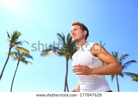 Sport man running Male athlete runner jogging in compression t-shirt top training on palm trees beach Fit handsome male fitness model jogging alone training for marathon run Man in his twenties Sport man running Male athlete runner jogging in compression t-shirt top training on palm trees beach Fit handsome male fitness model jogging alone training for marathon run Man in his twenties