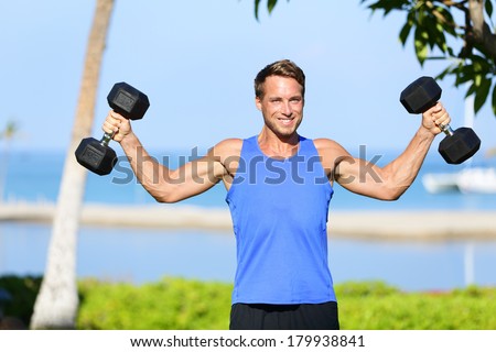 Weight training Fitness man with dumbbell weights in workout outside. Fit muscular male lifting weights in shoulder press exercise. Sports model exercising outdoor in summer. Handsome Caucasian man.