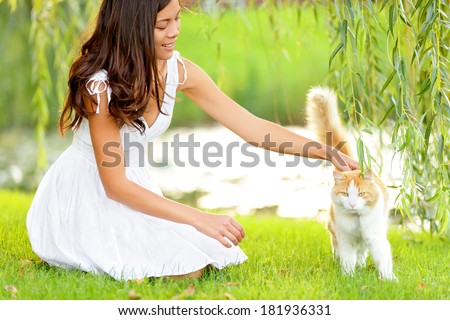 Woman petting cat in summer park. Happy cute girl playing with adorable cats in city park during spring or summer. Beautiful mixed race Asian Caucasian female model smiling happy outdoors.