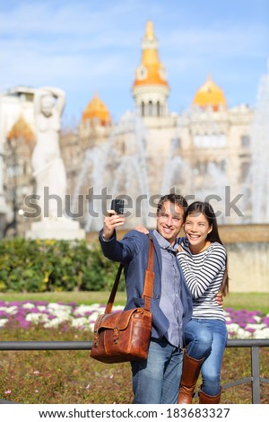 Tourist travel couple taking selfie in Barcelona with smart phone camera. Trendy cool urban city couple, Cauasian man, Asian woman traveling together, Placa de Catalunya, Catalonia Square, Barcelona