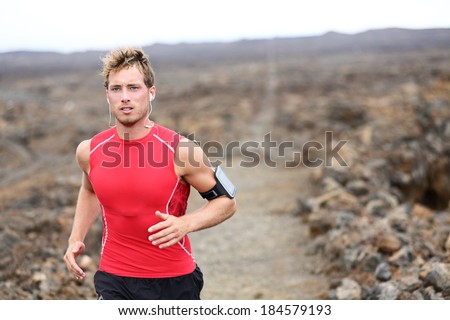 Man running - trail runner cross country training outdoors for marathon or triathlon ironman. Handsome male athlete working out on Hawaii, Big Island, USA. Triathlete listening to music on smart phone