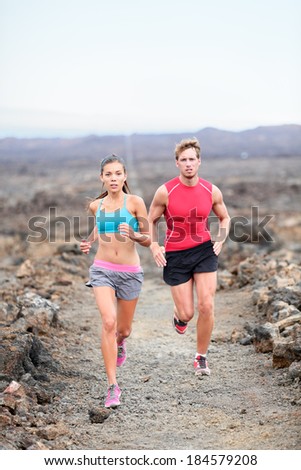 Runners couple running on trail in cross country run outdoors training for marathon or triathlon. Fit young fitness model man and asian woman training together outside on Big Island, Hawaii, USA.