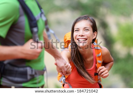 Helping hand - hiking woman getting help on hike smiling happy overcoming obstacle. Active lifestyle hiker couple traveling. Beautiful smiling mixed race Asian Caucasian female model.