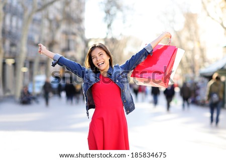 Shopping woman excited happy on La Rambla street in Barcelona. Shopper girl holding shopping bags up excited outdoors on walking street. Mixed race Asian Caucasian female model cheerful in Spain.