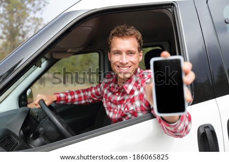 Smartphone man in car driving showing smart phone display smiling happy. Male driver using app showing blank empty screen sitting in drivers seat. Focus on model.