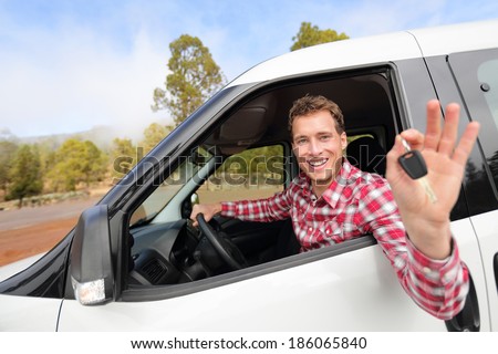 New cars - man driving car showing car keys happy looking at camera. Male driver on road trip in beautiful landscape nature. Focus on model.