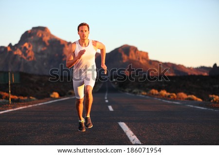 Athlete running sprinting at sunset on road. Male runner training in mountain landscape at night. Fit young muscular fitness sport model in his 20s.