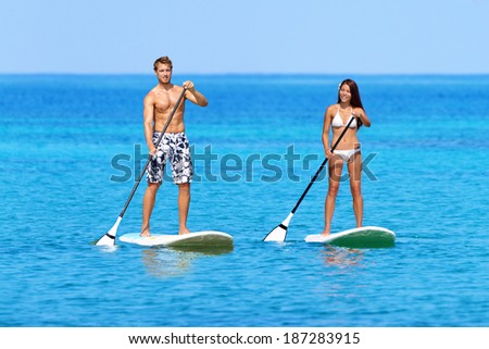 Stand up paddleboarding beach people on stand up paddle board, SUP surfboard surfing in ocean sea on Big Island, Hawaii Beautiful young mixed race Asian woman and Caucasian man doing water sport.