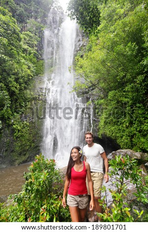 Hawaii tourist hiking people. Couple happy by waterfall during travel on the road to Hana on Maui, Hawaii. Ecotourism concept image with happy backpackers. Interracial Asian / Caucasian young couple.
