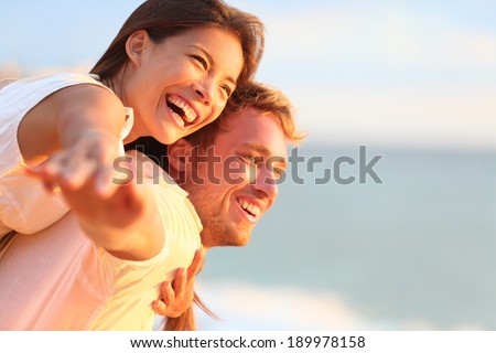 Beach couple laughing in love romance on travel honeymoon vacation summer holidays romance. Young happy people, Asian woman and Caucasian man embracing outdoors on tropical beach in casual wear.
