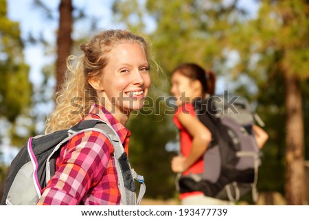Hiking woman portrait smiling happy in forest. Female hiker girl trekking wearing backpack outside looking candid and fresh at camera. Beautiful young blonde girl living healthy lifestyle.
